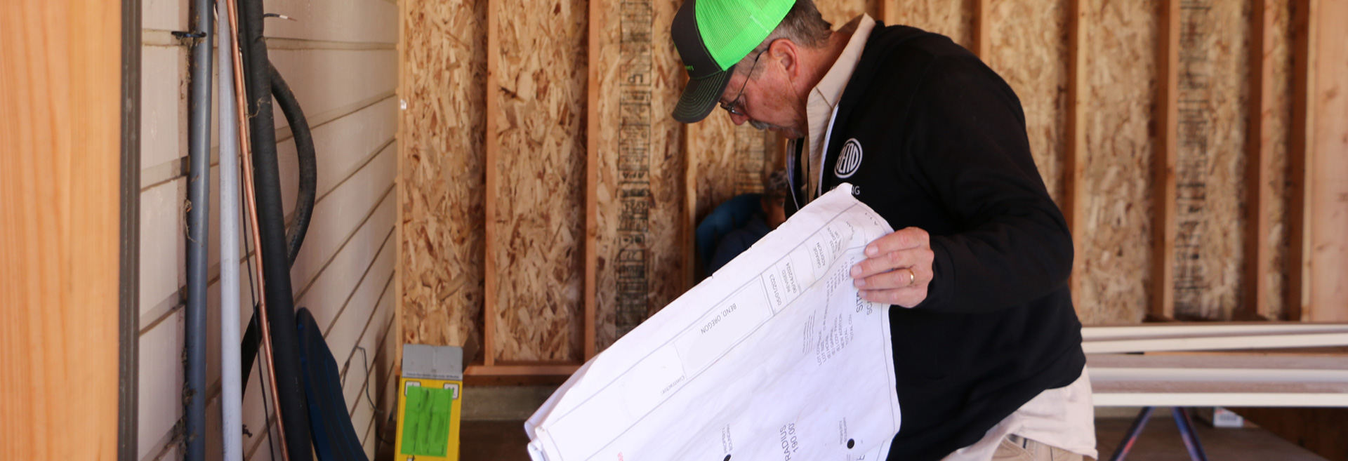 Building inspector with a black and green hat looking at a set of blueprints