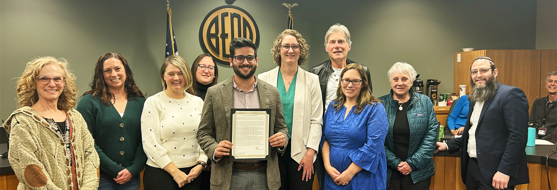 Gorup of diverse people standing with council members in front of the council diesis in Council Chambers. 