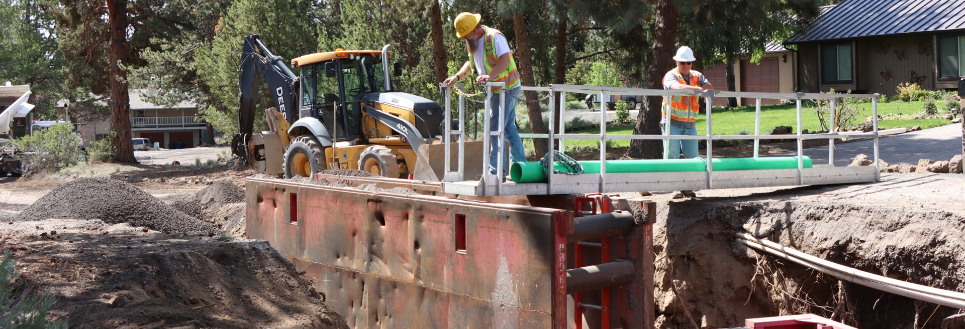 Construction workers working in a ditch using a backhoe in a street.