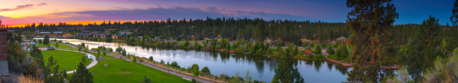 Panoramic view of Bend at sunrise looking east. Deschutes River in the foreground, trees, streets, houses.