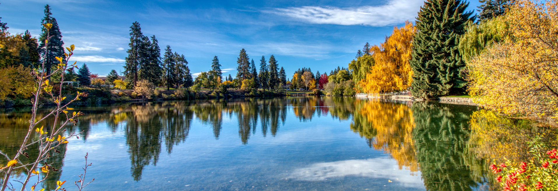 Deschutes River during fall. Clear water with colorful trees on the banks, sky is blue in the background.