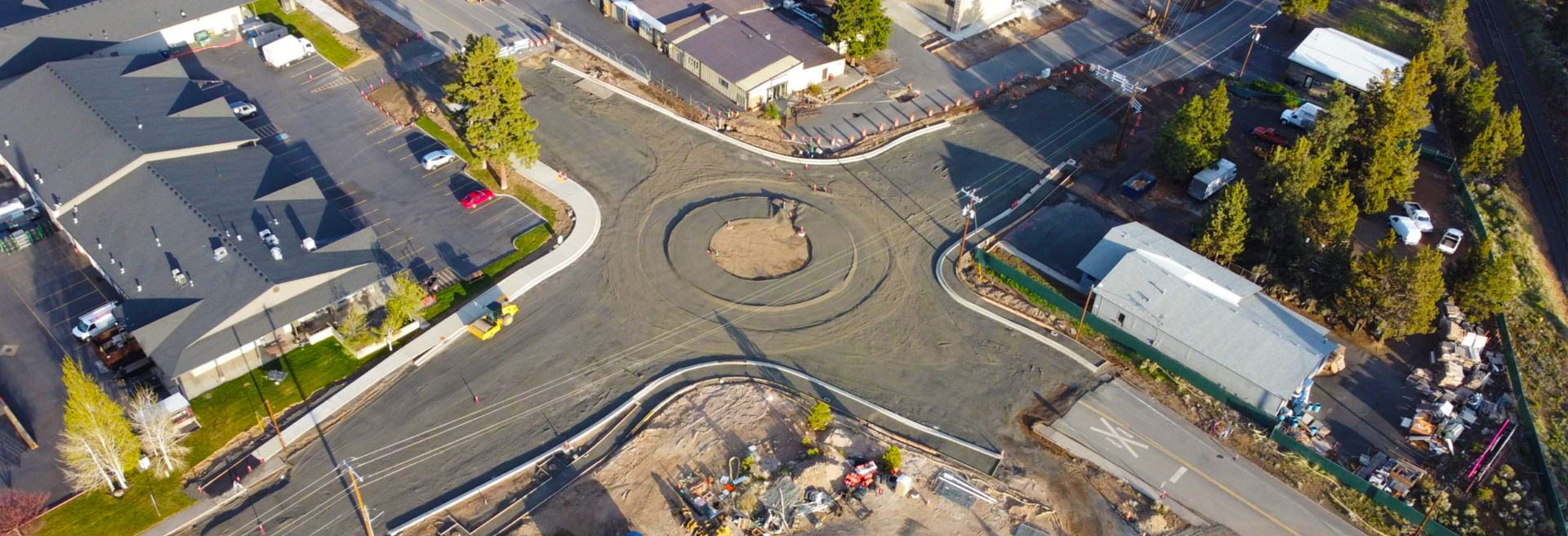 Drone shot of a roundabout traffic circle under construction. Buildings and trees surround the traffic circle.
