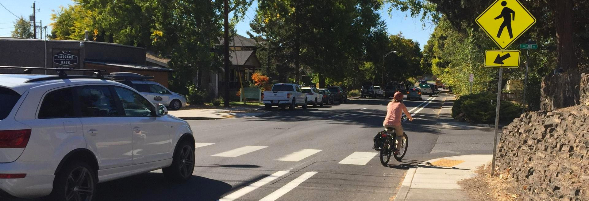 City street with cars driving a a bicyclist turning onto a side street.