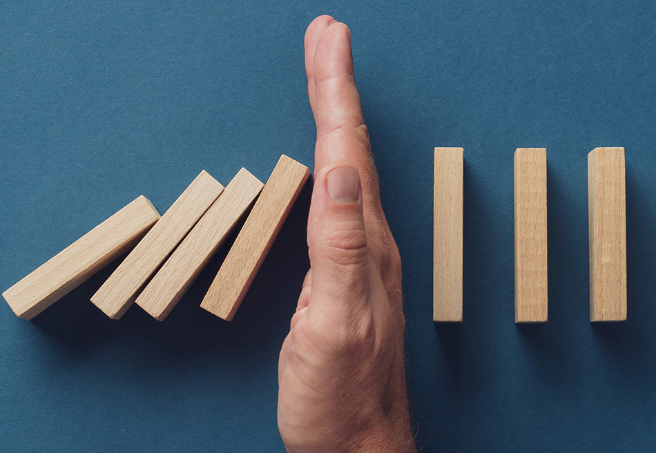Dominoes falling with a hand stopping them on a blue background.