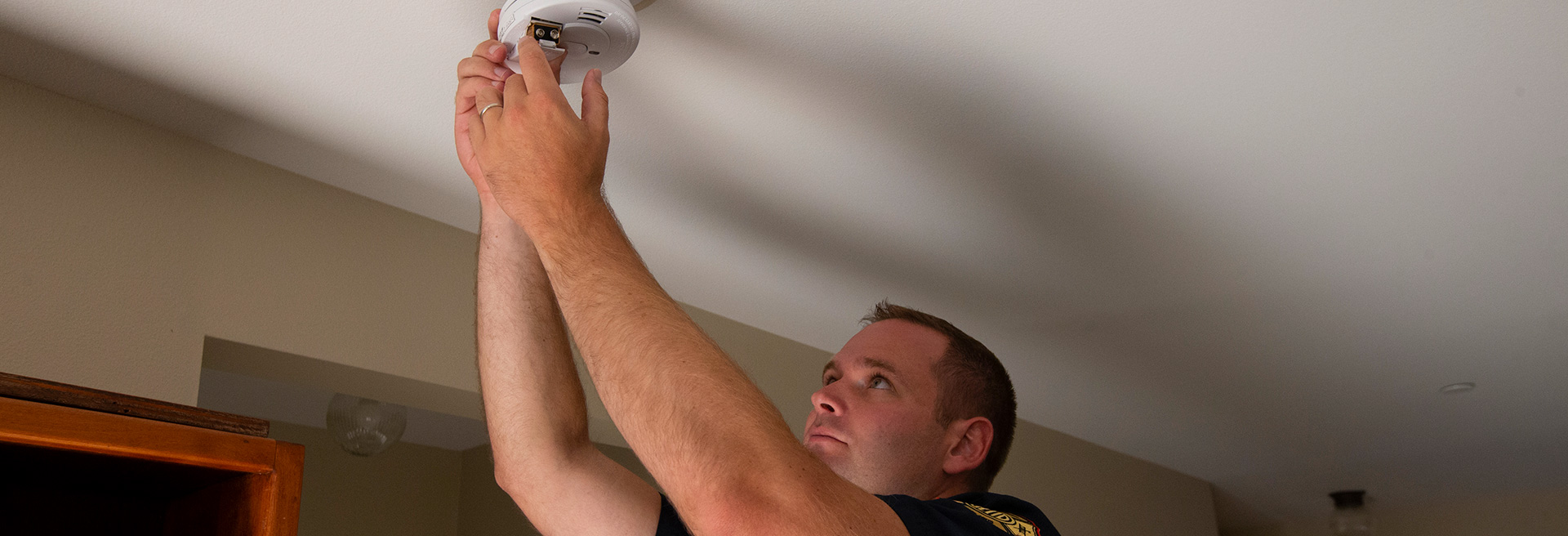 Man installing a smoke detector on the ceiling of a home.